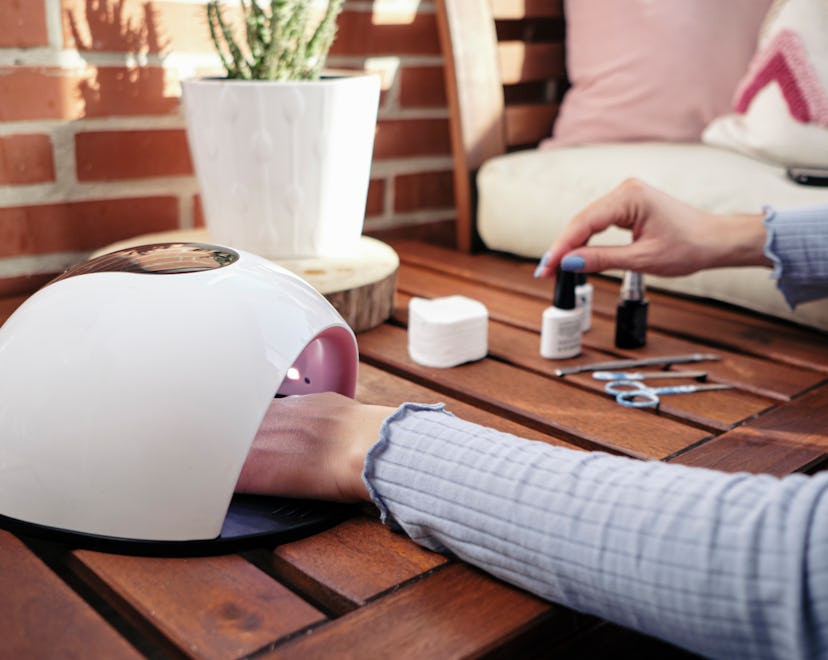 A woman applies a treatment to paint her fingernails blue on a wooden table