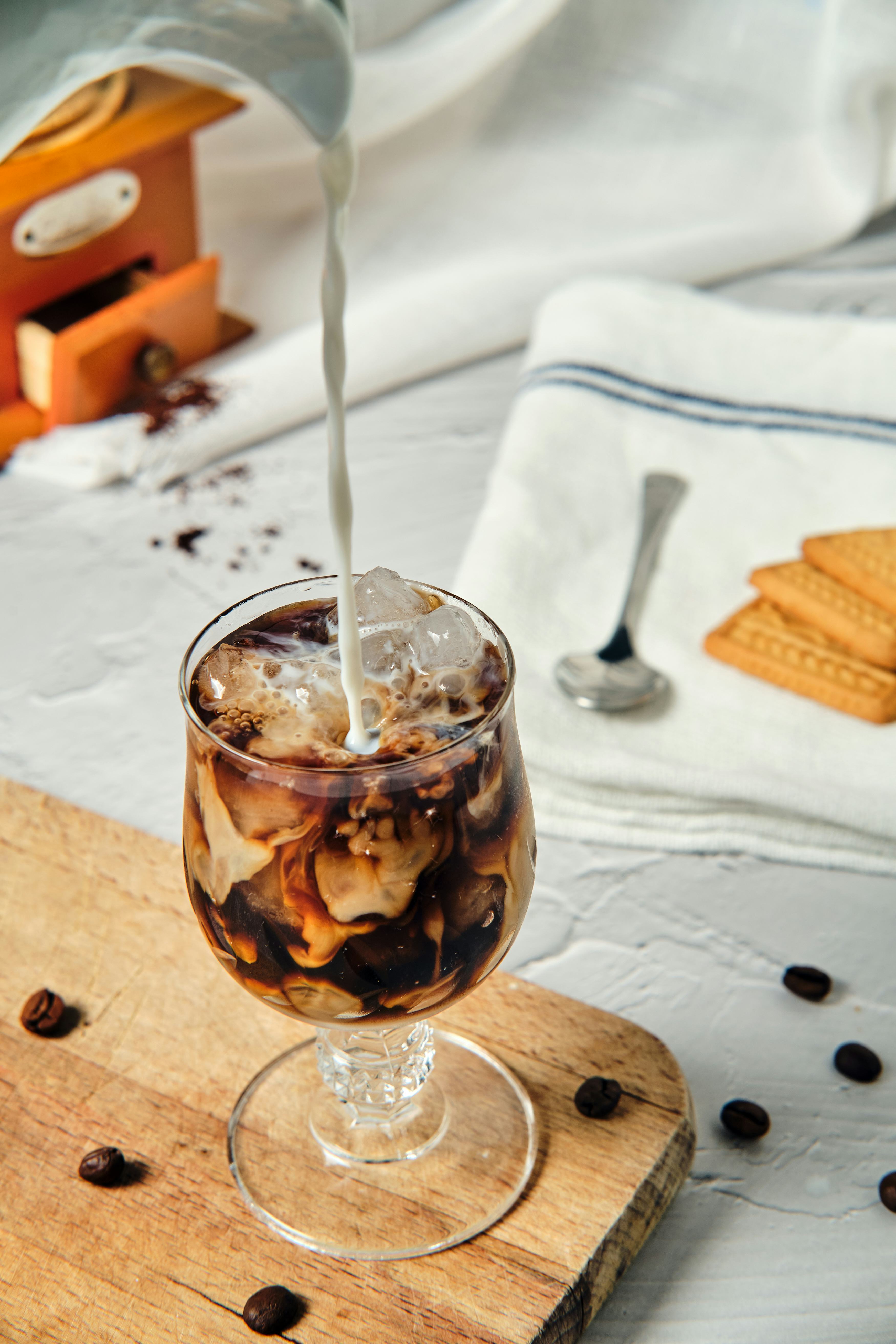 still life of cold coffee pouring milk with pitcher into a glass with coffee and mixing its colors