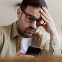 Worried man reading a problematic text message on cell phone at home.