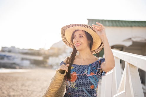 Mature woman is ready to enjoy the beach during a beautiful summer day, has a knitted straw hat