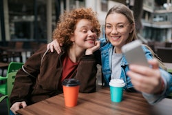 Two friends having fun at an outdoor coffee shop and taking a selfie. Common Gemini-Cancer cusp trai...
