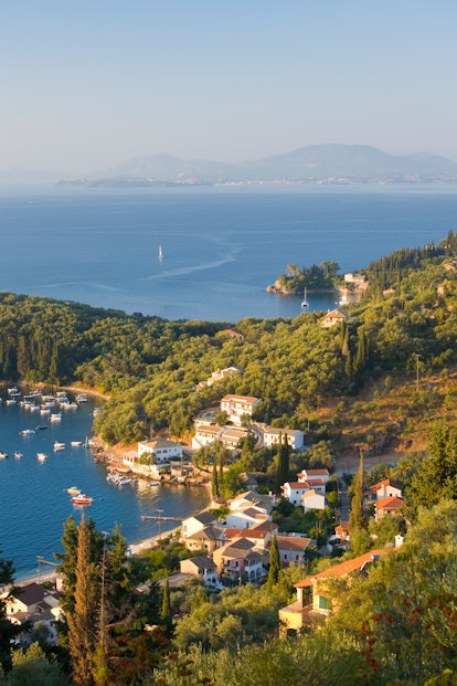 View from hillside over the village to the Strait of Corfu and distant Corfu Town, Kalami, Corfu (ak...