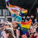 WROCLAW, POLAND - 2022/06/11: A young boy carried on his father shoulders waves a pride flag during ...