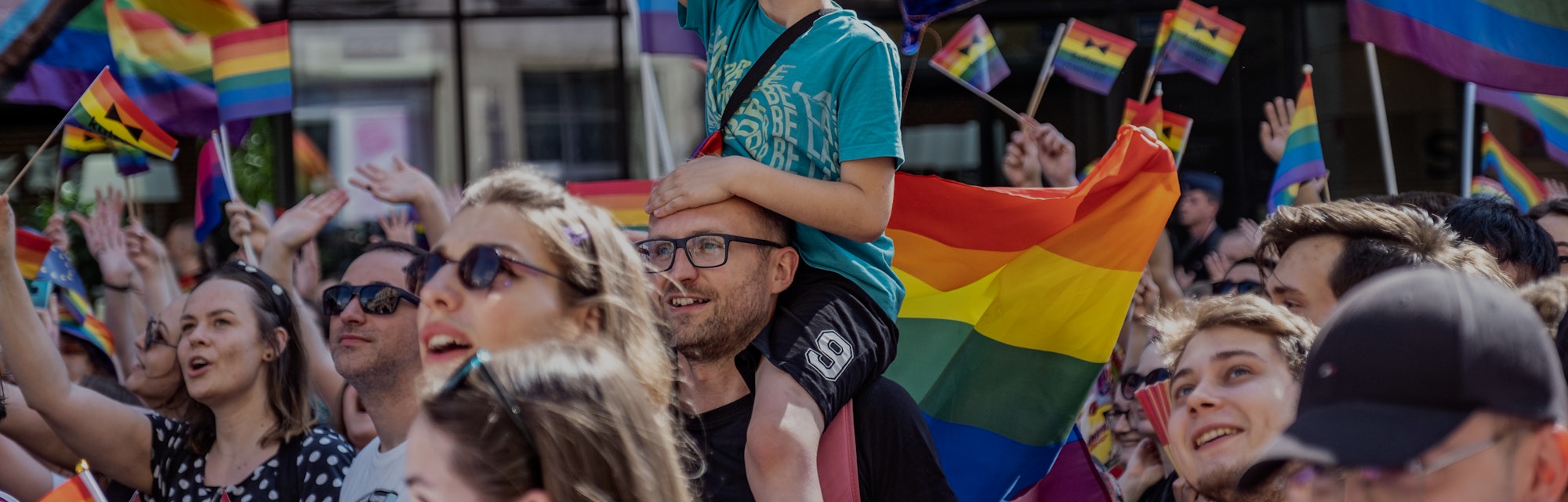 WROCLAW, POLAND - 2022/06/11: A young boy carried on his father shoulders waves a pride flag during ...