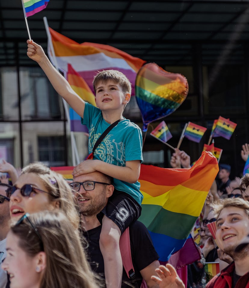 WROCLAW, POLAND - 2022/06/11: A young boy carried on his father shoulders waves a pride flag during ...