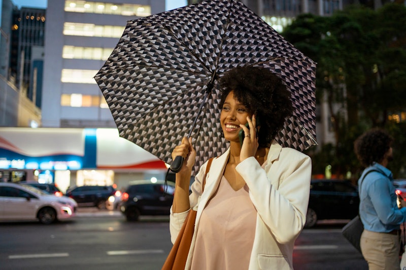 Portrait of woman talking on the smartphone with umbrella  at Avenida Paulista, São Paulo, Brazil.