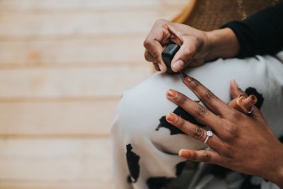 A black woman with long, slender fingers, paints her nails a shade of brown.