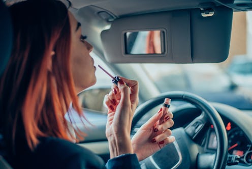Young business woman putting a lip gloss in the front seat of a car
