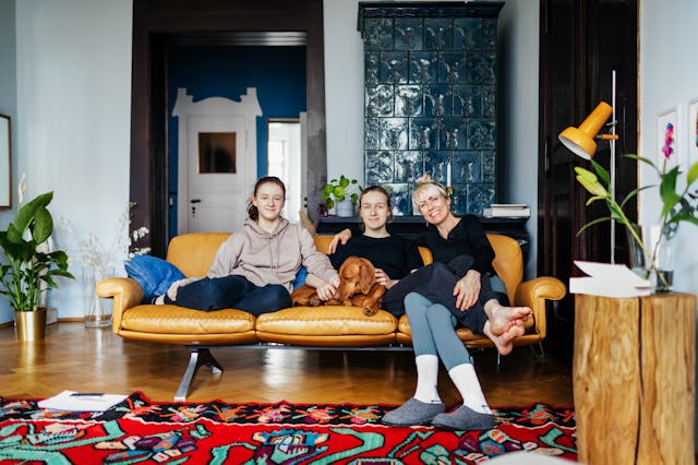 A portrait of a single mom sitting with her two daughters on a couch in their living room at home to...