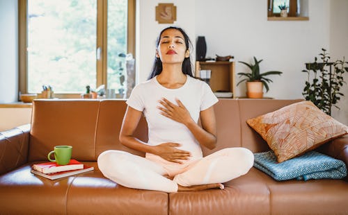 A woman meditates on a couch. Here's your june 16 zodiac sign daily horoscope.