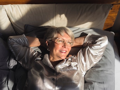 A happy 90-year-old woman lying in bed and smiling while looking towards her window