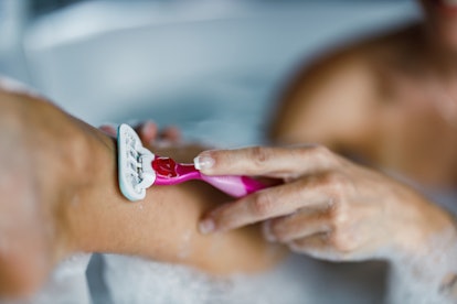 Close up of unrecognizable woman shaving leg with razor during morning bath in the bathroom.