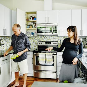 Pregnant couple unloading dishwasher in home kitchen together