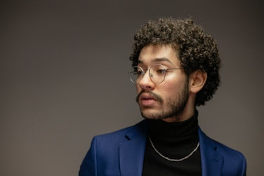 A young man with a short afro hairstyle wearing glasses and a formal suit