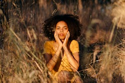 A woman sits pensively in a field. here's how cancer season 2022 will affect each zodiac sign.