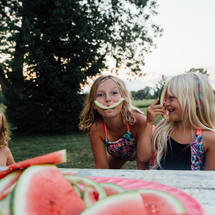 Three girls of millennial parents playing with rinds of eaten watermelon slices outside
