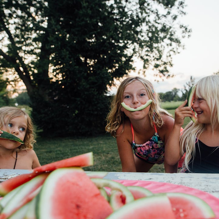 Three girls of millennial parents playing with rinds of eaten watermelon slices outside