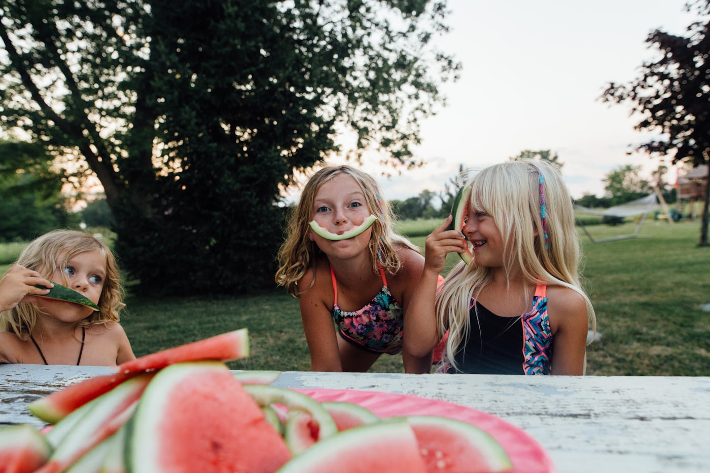 Three girls of millennial parents playing with rinds of eaten watermelon slices outside