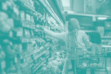 一位年轻的穆斯林母亲和女儿一起走在杂货店的农产品过道上。