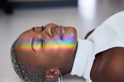 Close-up of a ray of rainbow colored light refracting onto a the face of a woman lying on a floor wi...