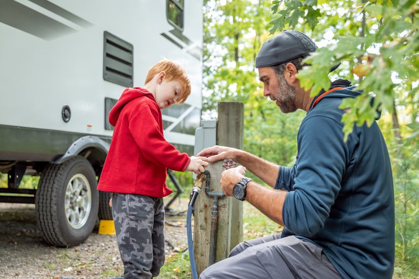 A father and son connect camper trailer hoses at a campsite. Researching campsite amenities like RV ...