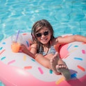 Girl holding juice when sitting comfortably in a donut shaped floater in swimming pool