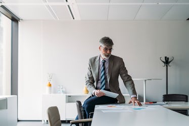 A man sitting on his desk pointing and looking at his papers