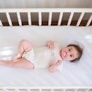 Baby in an empty crib, on their back with a pacifier in their mouth