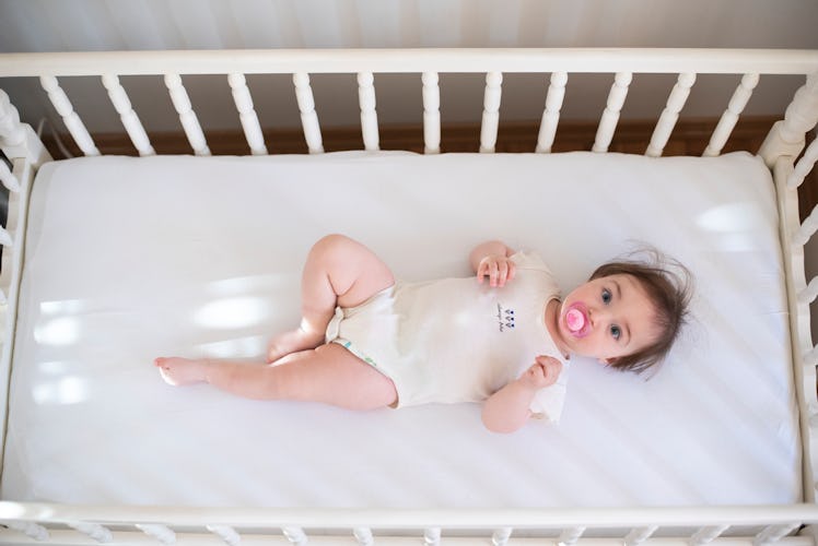 Baby in an empty crib, on their back with a pacifier in their mouth