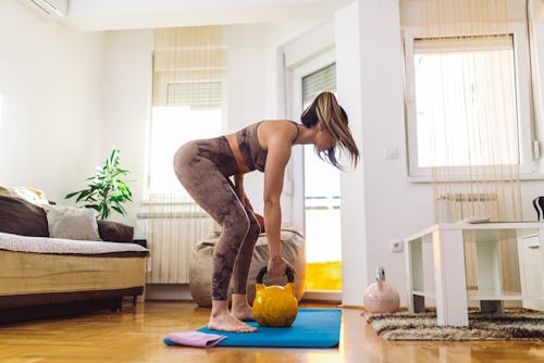 Woman exercising with weights in small living room at her home. She is mid adult, wearing sport tigh...