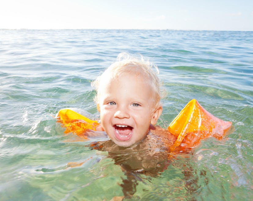 A blonde-haired boy swimming in the sea with arm floaties on