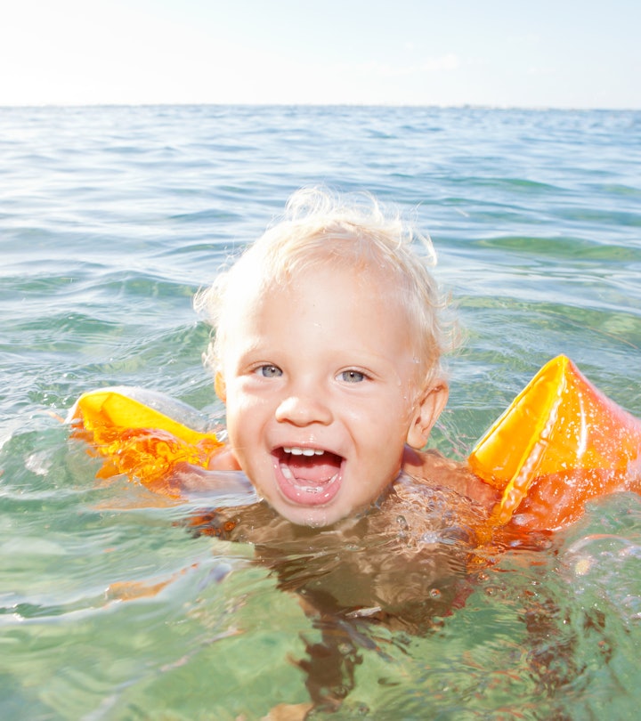 A blonde-haired boy swimming in the sea with arm floaties on