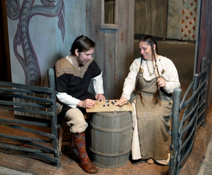 Keith Nelson and Rae Lundquist play a board game (Hnefatafl, it's called) in back of the Viking hous...