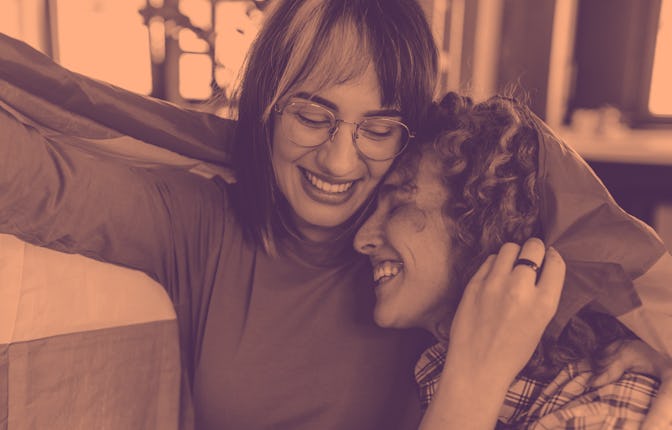 Close-up shot of a young lesbian couple at home holding a rainbow flag as a symbol of their LGBT rel...