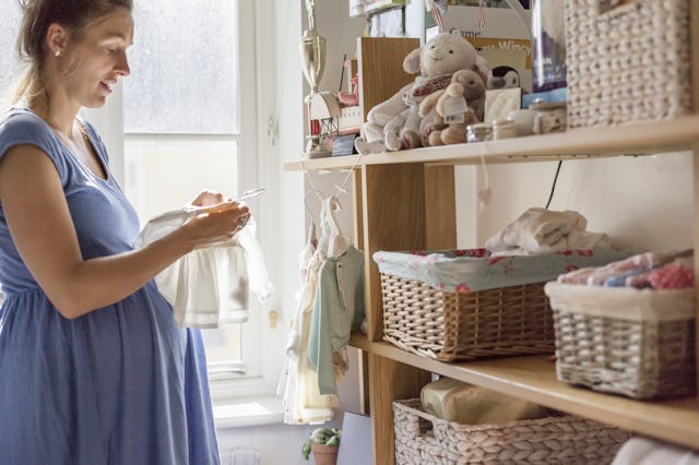 A pregnant blonde woman looking at the essential clothes for her baby in a sunny room