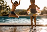 Back view of playful kids having fun while jumping into the swimming pool, pool safety tips for pare...