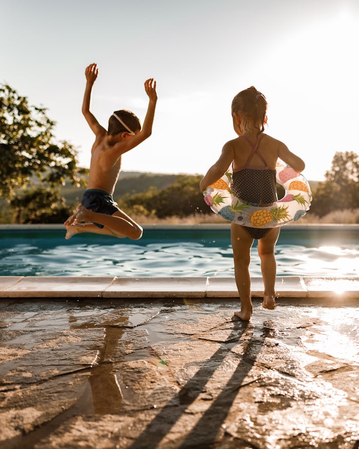Back view of playful kids having fun while jumping into the swimming pool, pool safety tips for pare...
