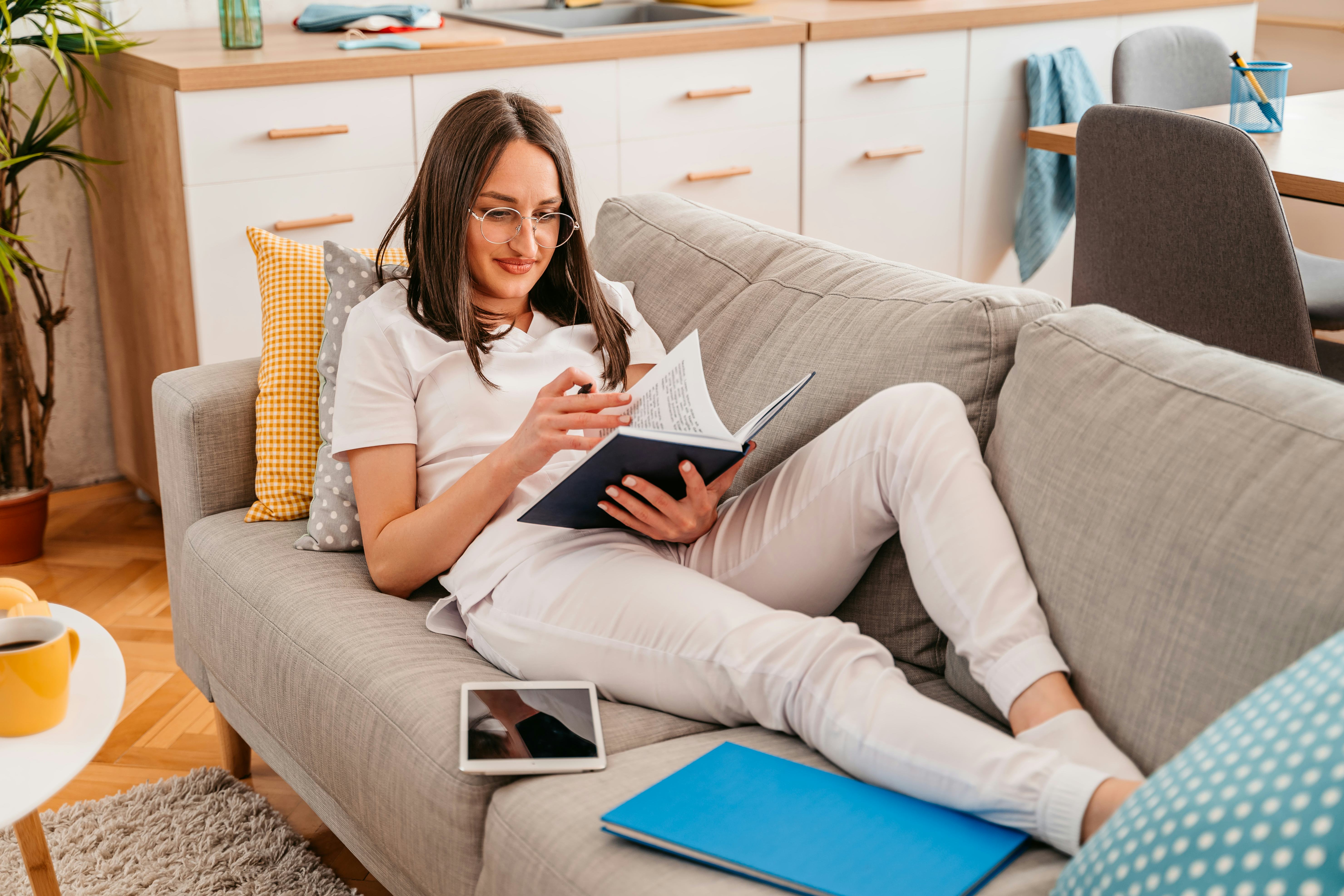 Beautiful young female student studying at home, sitting on the sofa.
