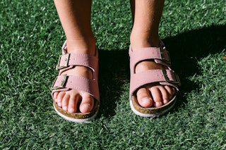 Detail front view of little girl's feet wearing pink buckle sandals on grass in natural light with h...