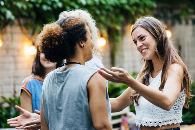 Two young women meeting at a barbecue with friends are greeting each other with excitement.