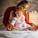 Little girl reading a bedtime story with her Mother in her bed. They are sitting together and the li...