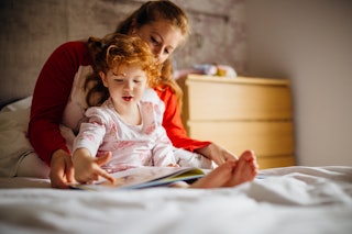 Little girl reading a bedtime story with her Mother in her bed. They are sitting together and the li...