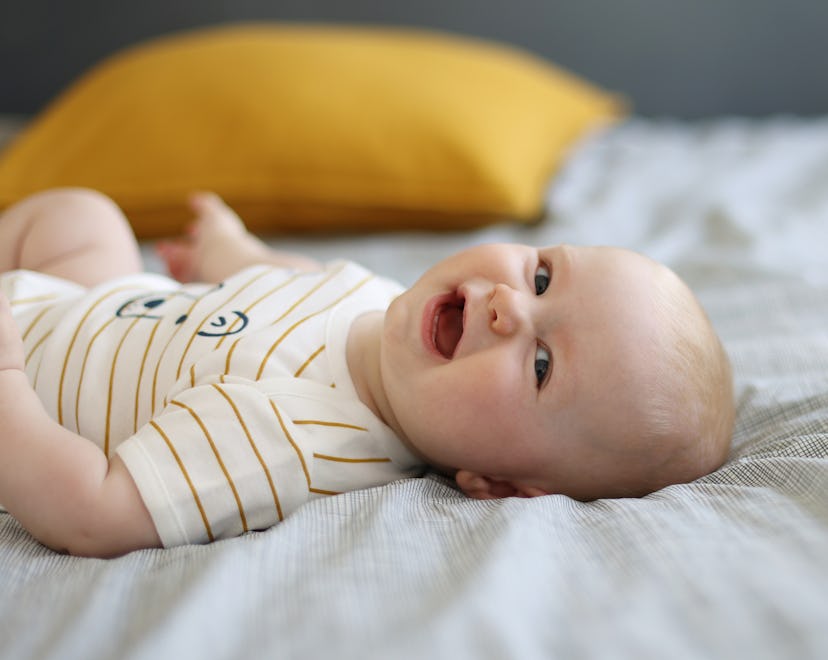 Happy baby boy laying on back with face toward camera, laughing, in article about boy names that sta...