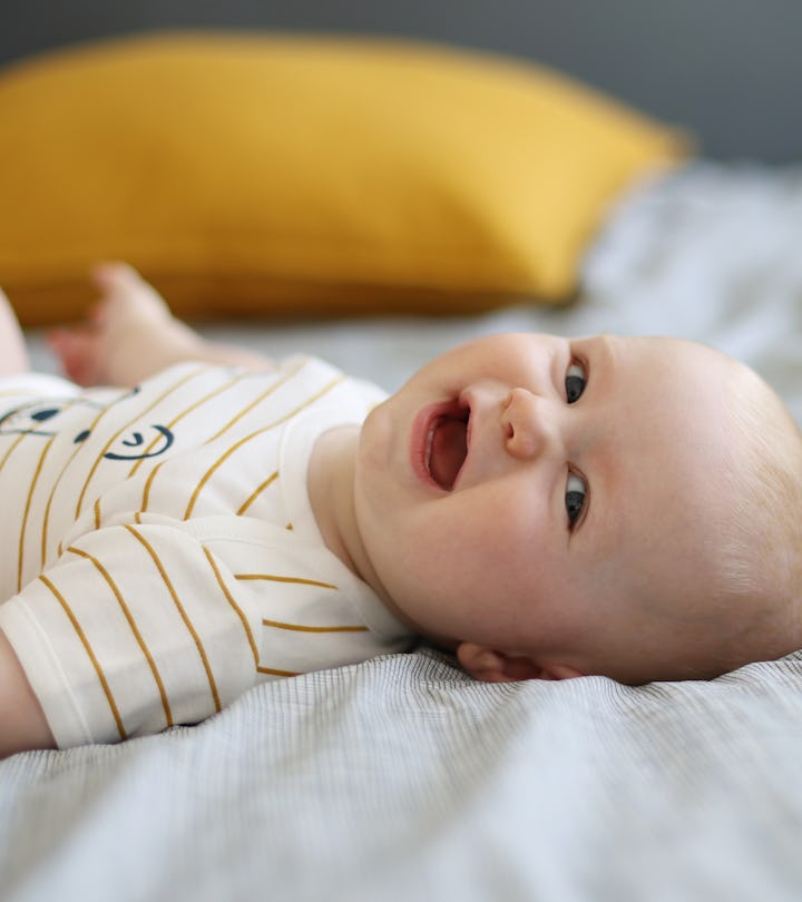 Happy baby boy laying on back with face toward camera, laughing, in article about boy names that sta...