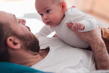 A dad on a couch holding his baby to his chest.