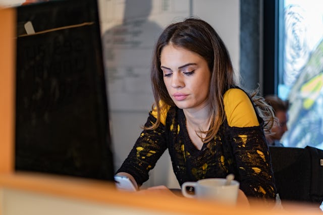 Young female programmer text messaging on smart phone while working in the office.