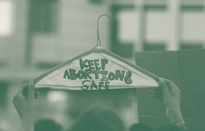 A person holds a metal coat hanger, a symbol of the reproductive rights movement, with the words "Ke...