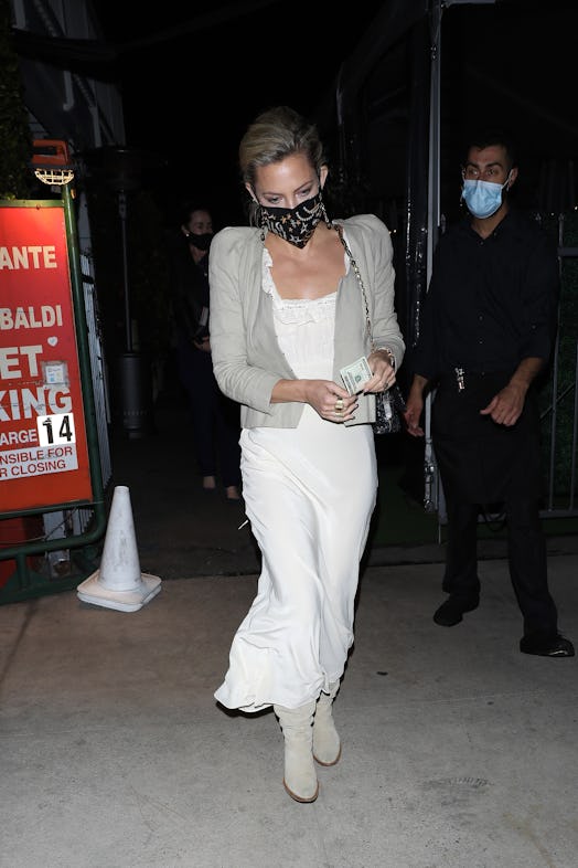 Kate Hudson wearing a white maxi dress with a taupe cardigan on top and matching boots