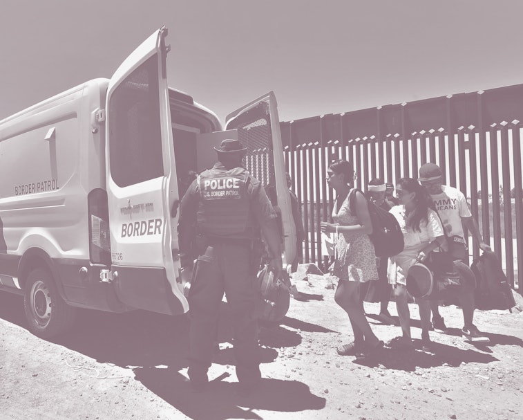 A US Customs and Border Protection (CPB) officer watches as migrants board a Border Patrol van to be...