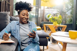 A woman uses a manifestation app on her phone while journaling.